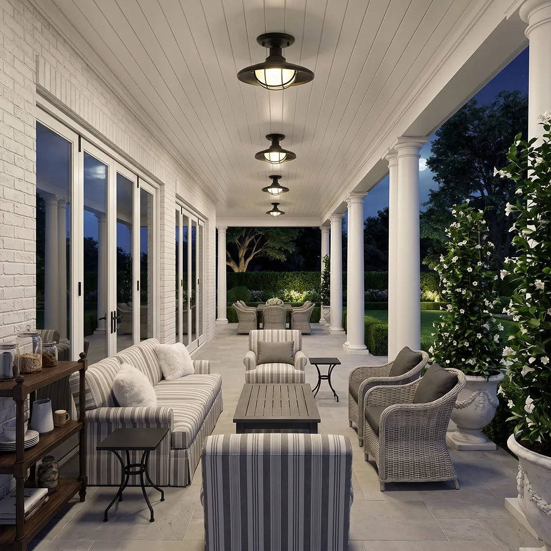 Black semi flush ceiling lights arranged along a long covered porch at night with cushioned lounge seating.