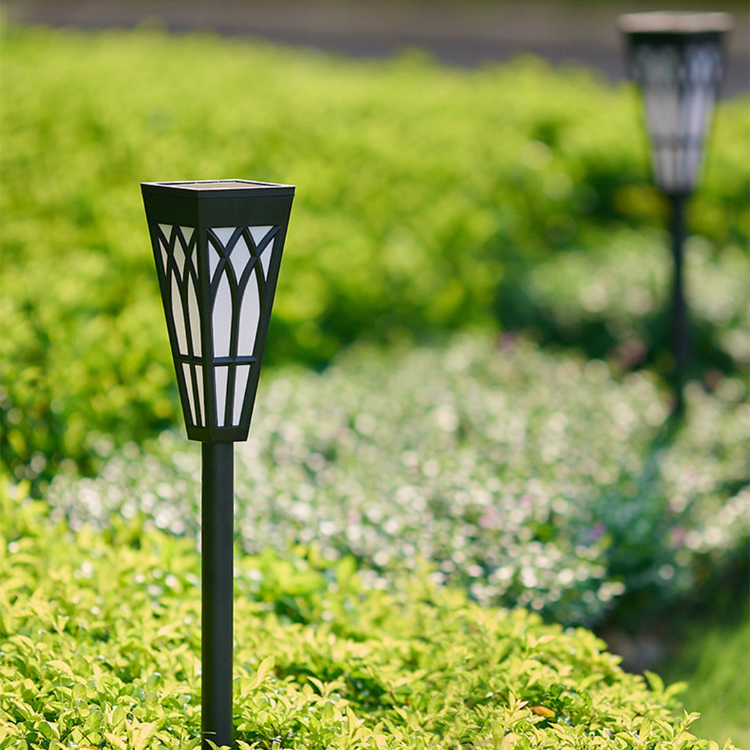 Black metal solar lights positioned among green garden foliage and flower beds