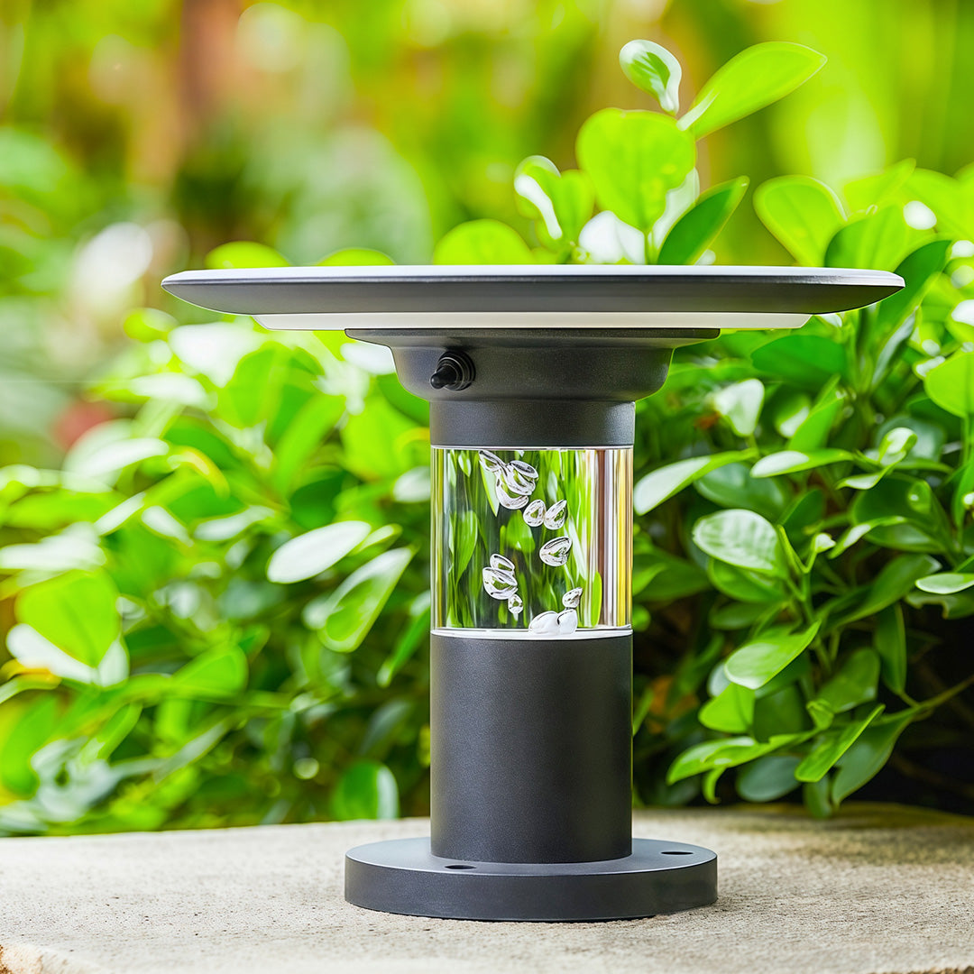 Black solar post cap light fixture showcasing its top solar panel, installed on a stone base in a garden.
