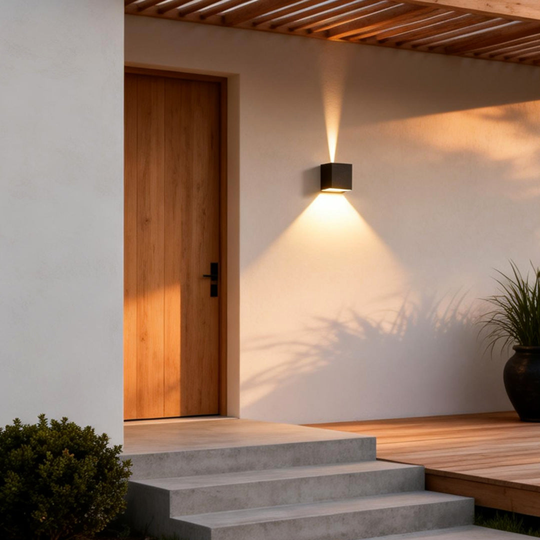 Black square outdoor wall lights illuminating a modern house entrance with warm directional glow.