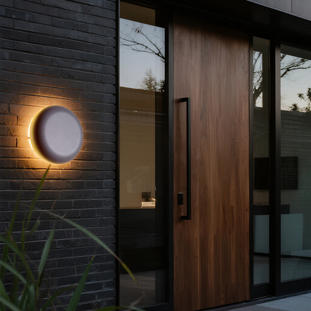 Black square waterproof outdoor wall light with golden halo effect on textured stone tile surface