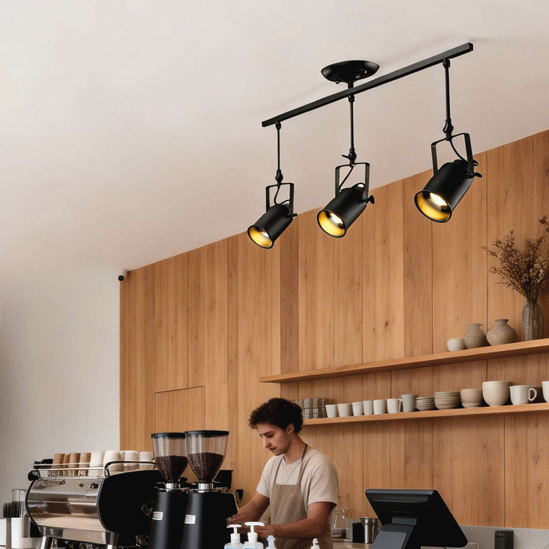 Black track light fixtures providing focused lighting for a barista workspace in a café.