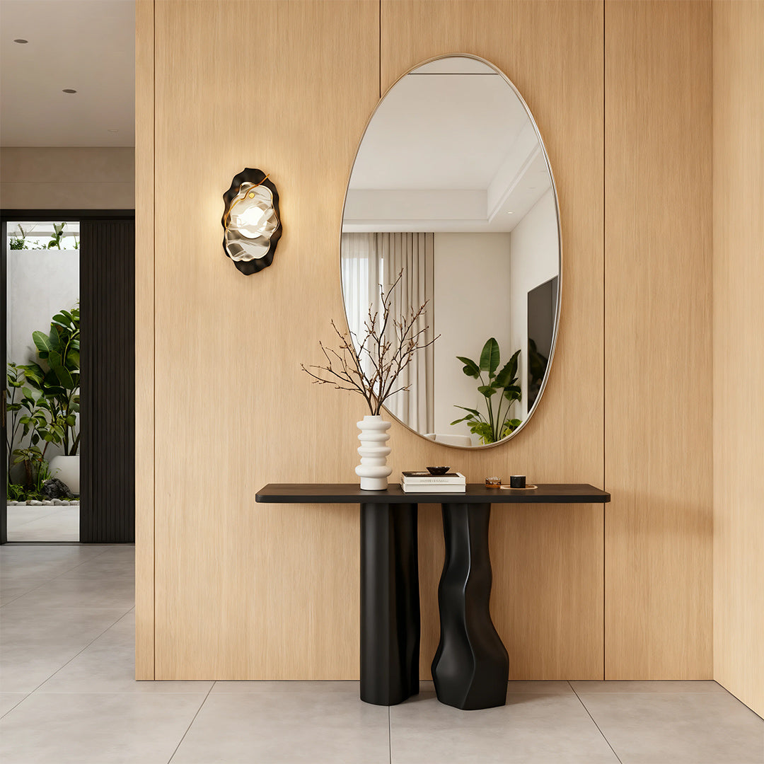 Black wall light brightening warm wood-paneled entryway with round mirror and console table