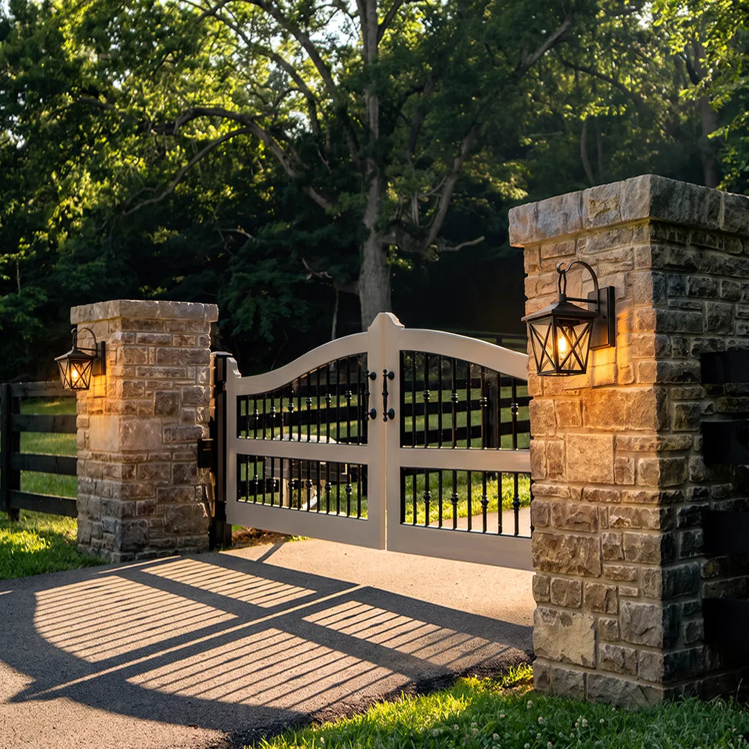 Black wall lighting installed on brick gate pillars, illuminating a residential driveway entrance with warm light.