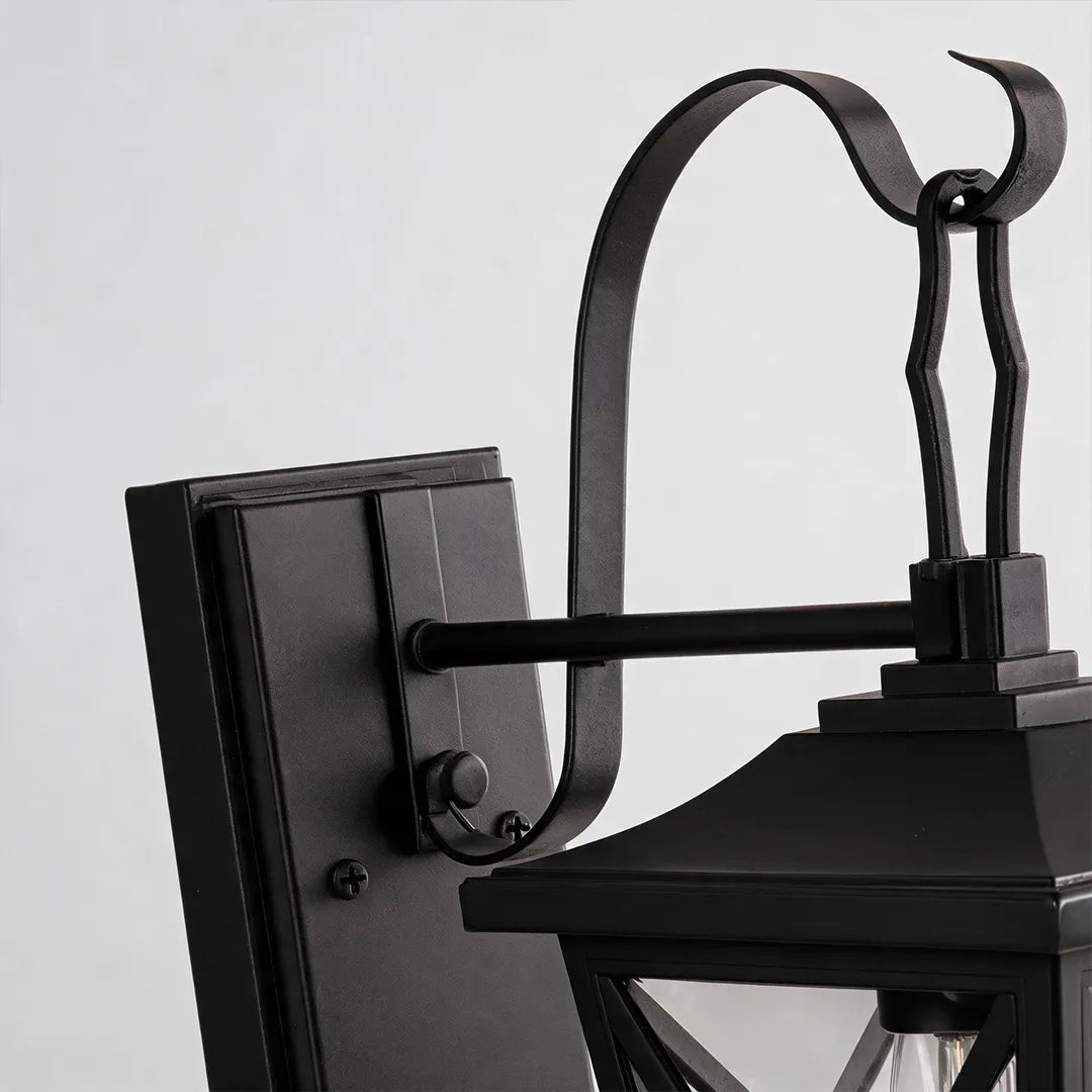Black wall lighting detail showing the curved mounting arm, rectangular backplate, and lantern top structure.