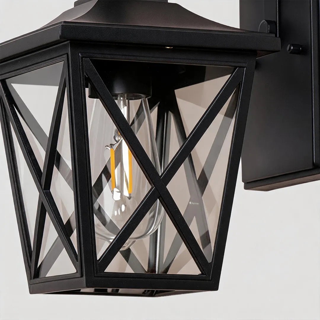 Black wall lighting close-up showing the geometric metal frame, clear glass panels, and exposed bulb detail.