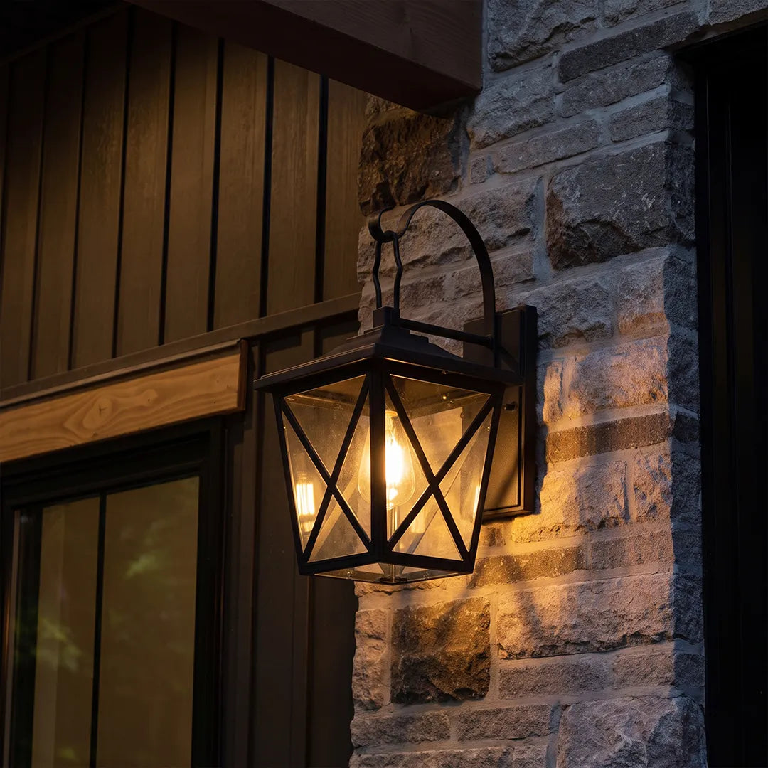 Black wall lighting mounted on a stone exterior wall beside a dark wood entry, featuring a geometric lantern design.