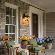 Black wall lighting mounted on a stone porch wall beside outdoor seating, creating a warm lantern-style glow.