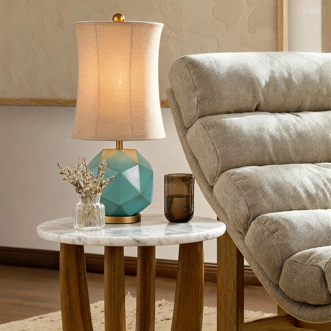 Modern industrial table lamps with a blue-green faceted ceramic base and natural textured linen shade on a round marble table.