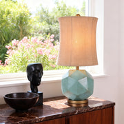 Modern industrial table lamps with a blue-green geometric faceted base, featuring brass accents and a burlap-textured shade on a dark wood cabinet.