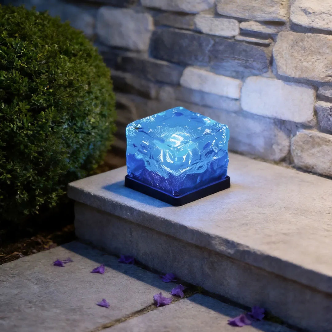 Blue outdoor ice cube light displayed on a concrete step near a stone wall for modern landscape decoration.