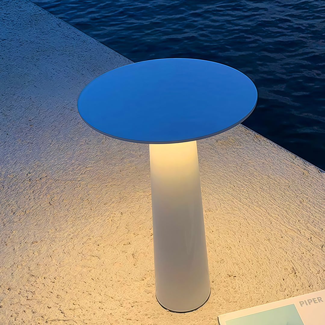 Blue-topped outdoor led table lamp creating soft illumination on a textured outdoor surface.