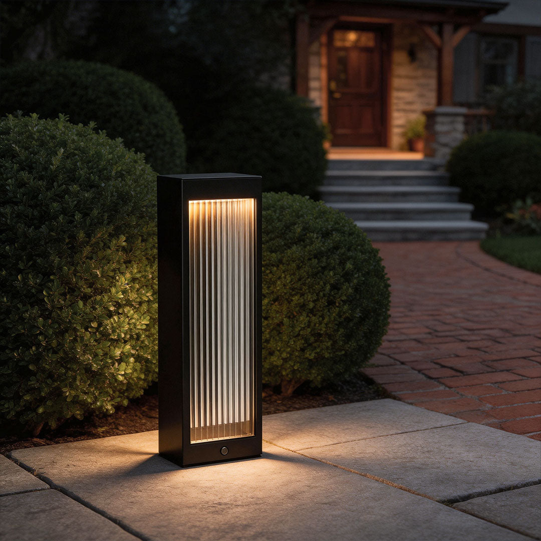 Bollard garden lights with a modern rectangular design, illuminating a pathway beside shrubs.