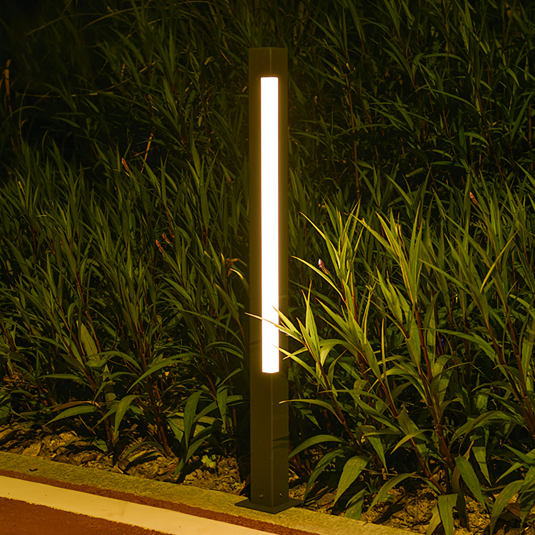Warm bollard landscape lighting placed beside dense greenery, providing vertical accent light at night.