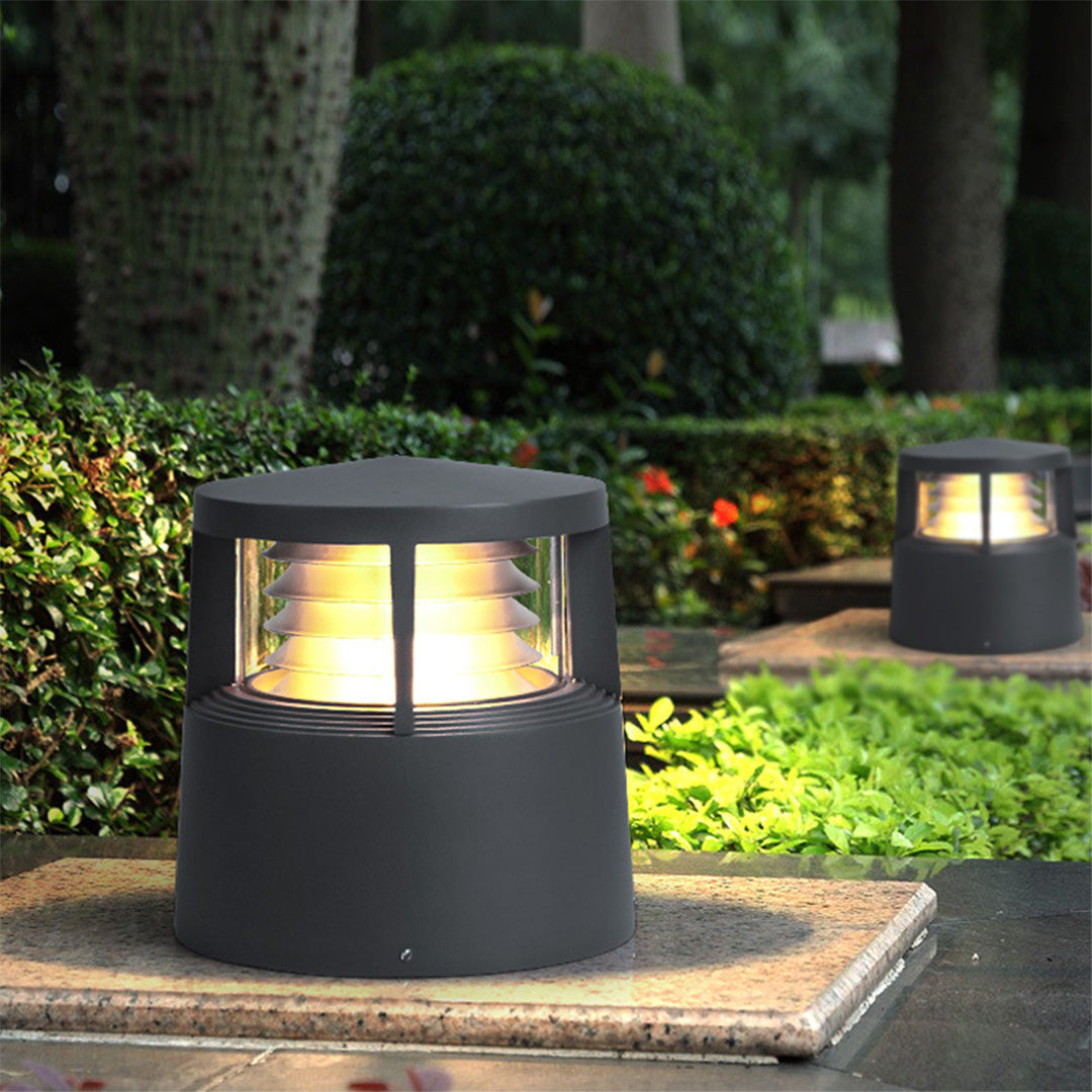 Warm-glow short bollard light installed on stone pedestal in landscaped garden