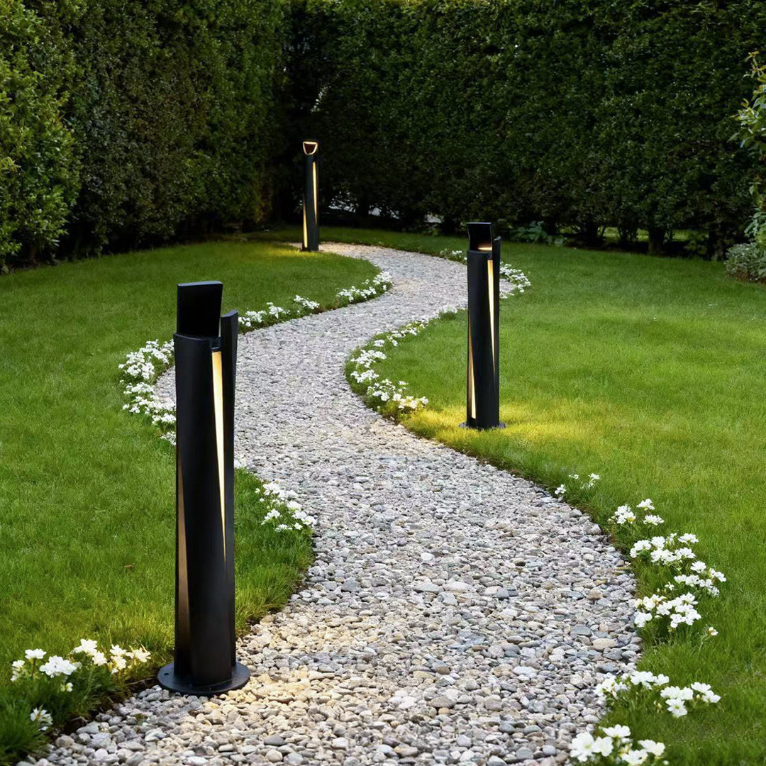 Bollard lighting fixtures lining curved gravel path through green lawn beside decorative flower borders