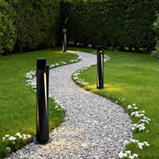Bollard lighting fixtures lining curved gravel path through green lawn beside decorative flower borders