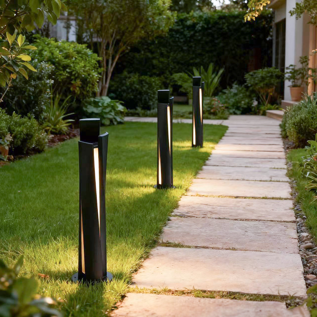 Bollard lighting fixtures guiding walkway beside grass with warm illumination in landscaped outdoor setting