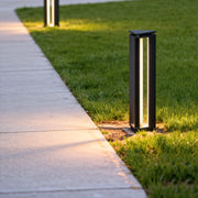Sleek bollard outdoor lights lining a concrete pathway with warm directional lighting during dusk.