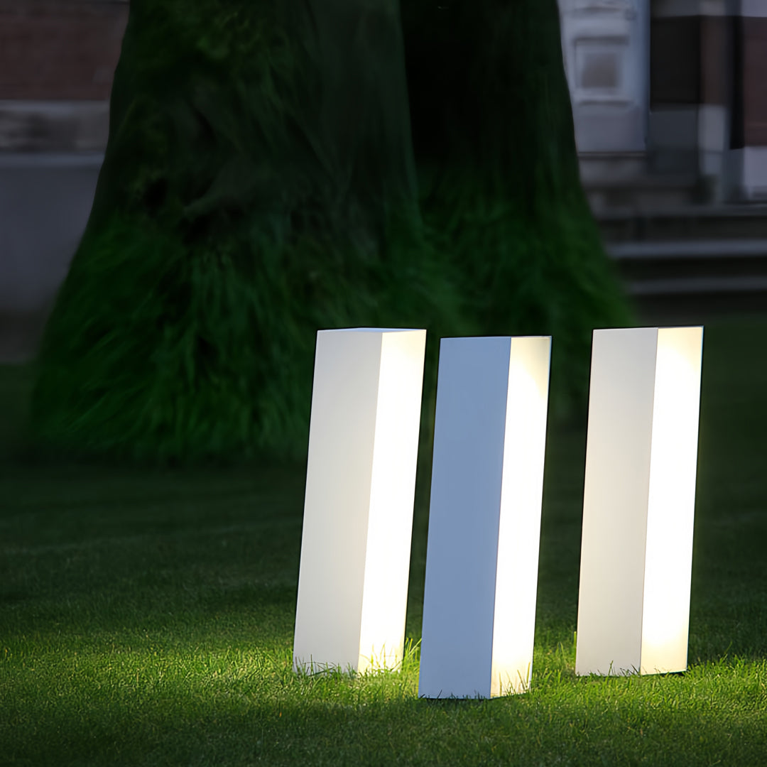 Three standing bollards with lighting installed in a grassy garden area with even diffused illumination.