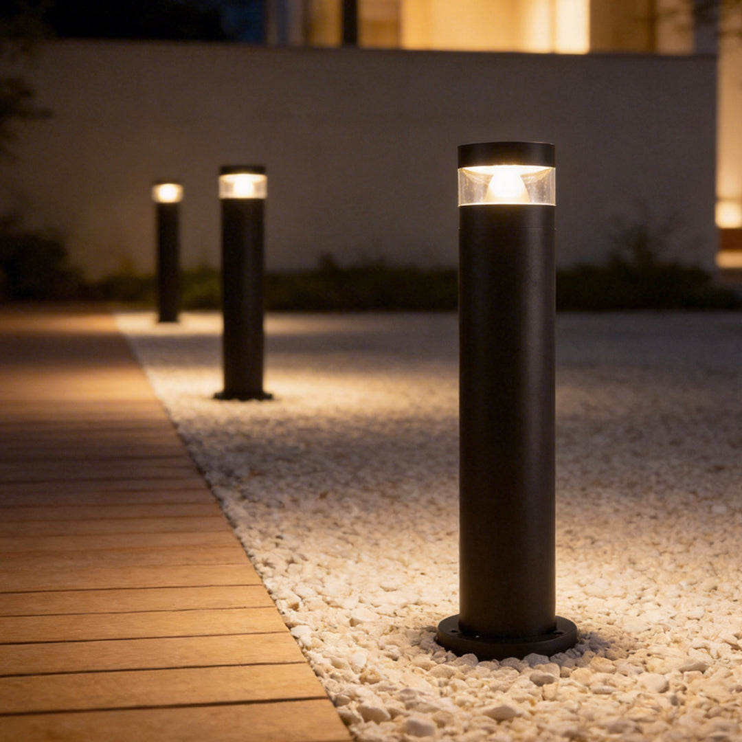 Bollards with lights illuminating a modern outdoor walkway beside wood decking and gravel.