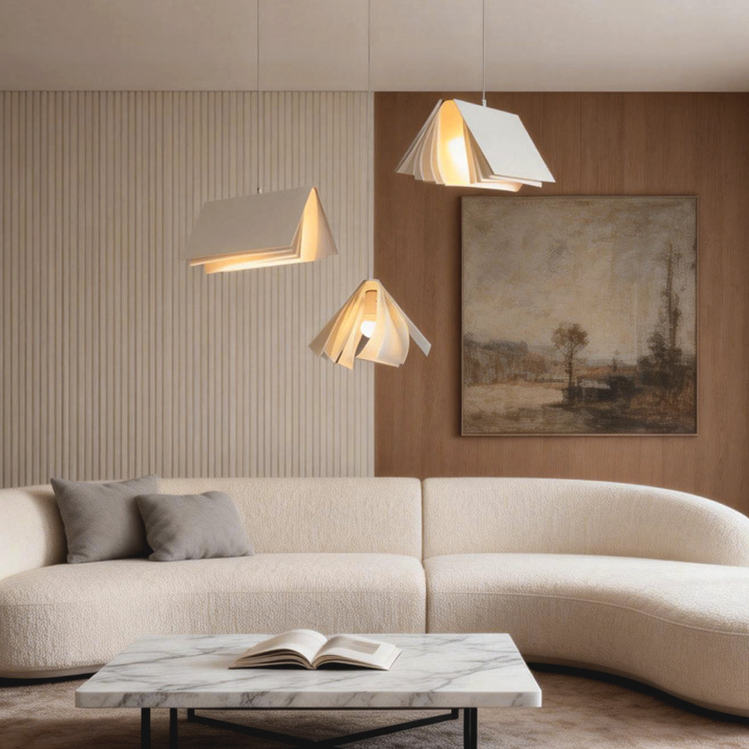 Contemporary book pendant light over a curved sofa seating area, creating soft layered lighting with sculptural book-like shades.