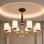 Brass candle chandelier with white shades installed in a modern dining room with elegant ambient lighting.