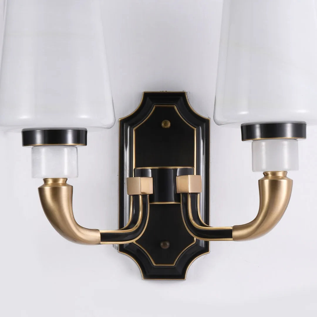 Brass candle sconces wall close-up showing black backplate, curved brass arms, and fabric shades.