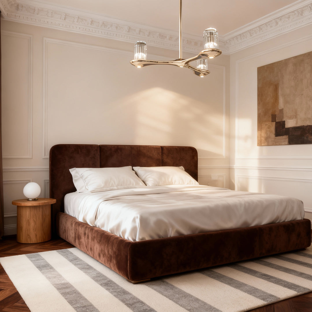 Brass crystal chandelier illuminating spacious bedroom with wooden bed frame and natural light from large windows