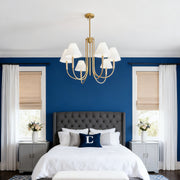 A brass finish cloth shade chandelier providing soft, ambient light in a stylish bedroom with a bold blue accent wall.