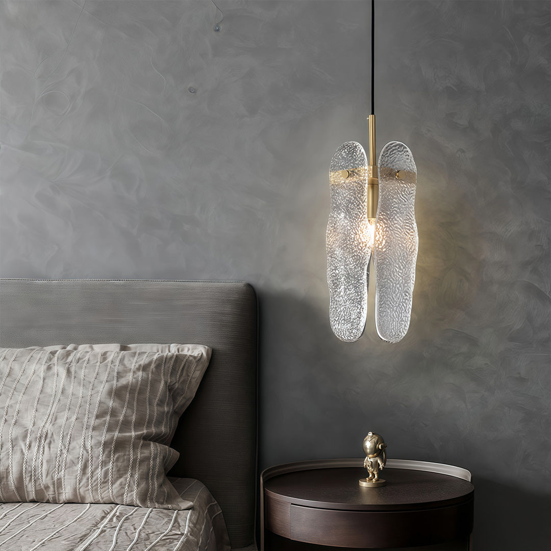 Brass glass pendant light illuminating modern grey bedroom with minimalist decor and bedside table.