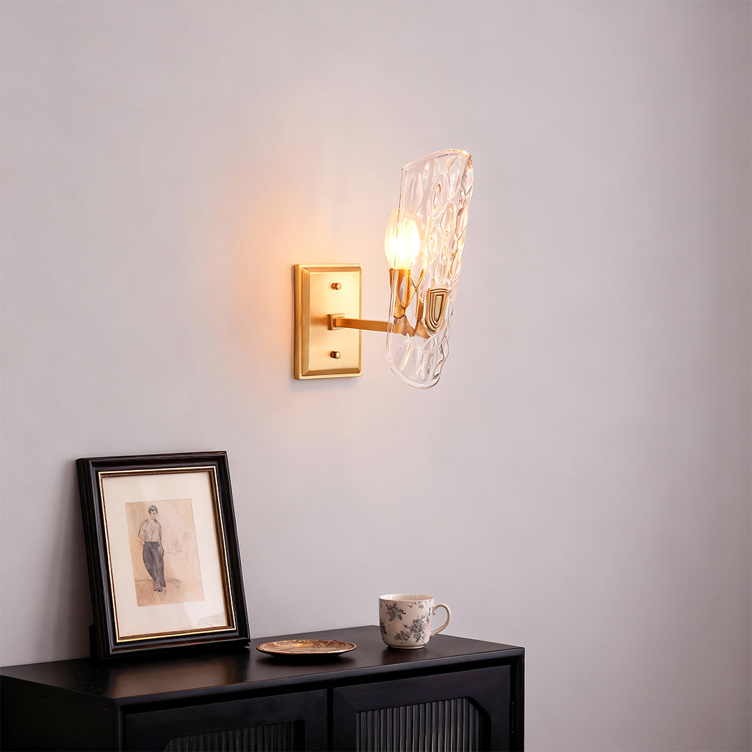 Brass glass wall light creating warm ambiance above black console with decorative items