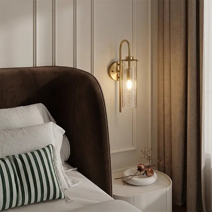 Brass glass wall sconce beside an upholstered bedroom bed