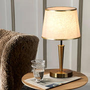 Modern brass table lamp positioned on wooden side table next to comfortable armchair