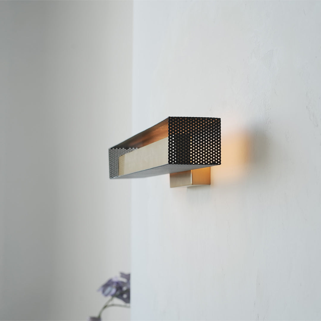 Brass wall light mounted on white wall, showcasing minimalist geometric style.