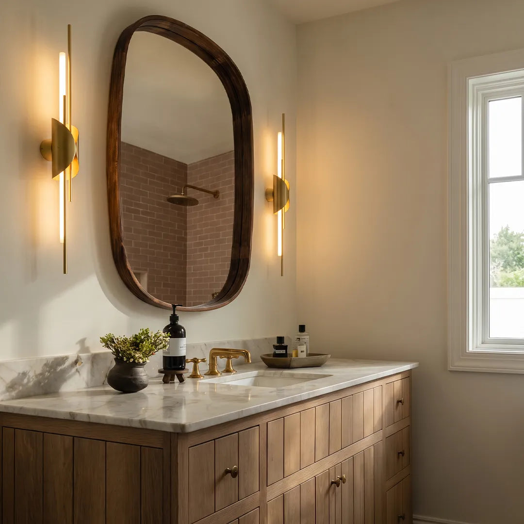 Brass wall sconce light installed on both sides of a bathroom mirror above a wood vanity.