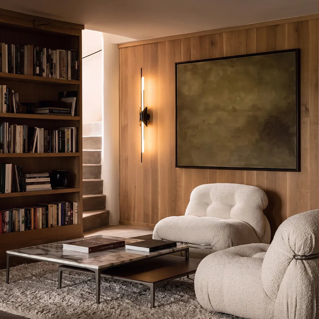 Brass wall sconce light adding warm glow to a modern living room with artwork and shelving.