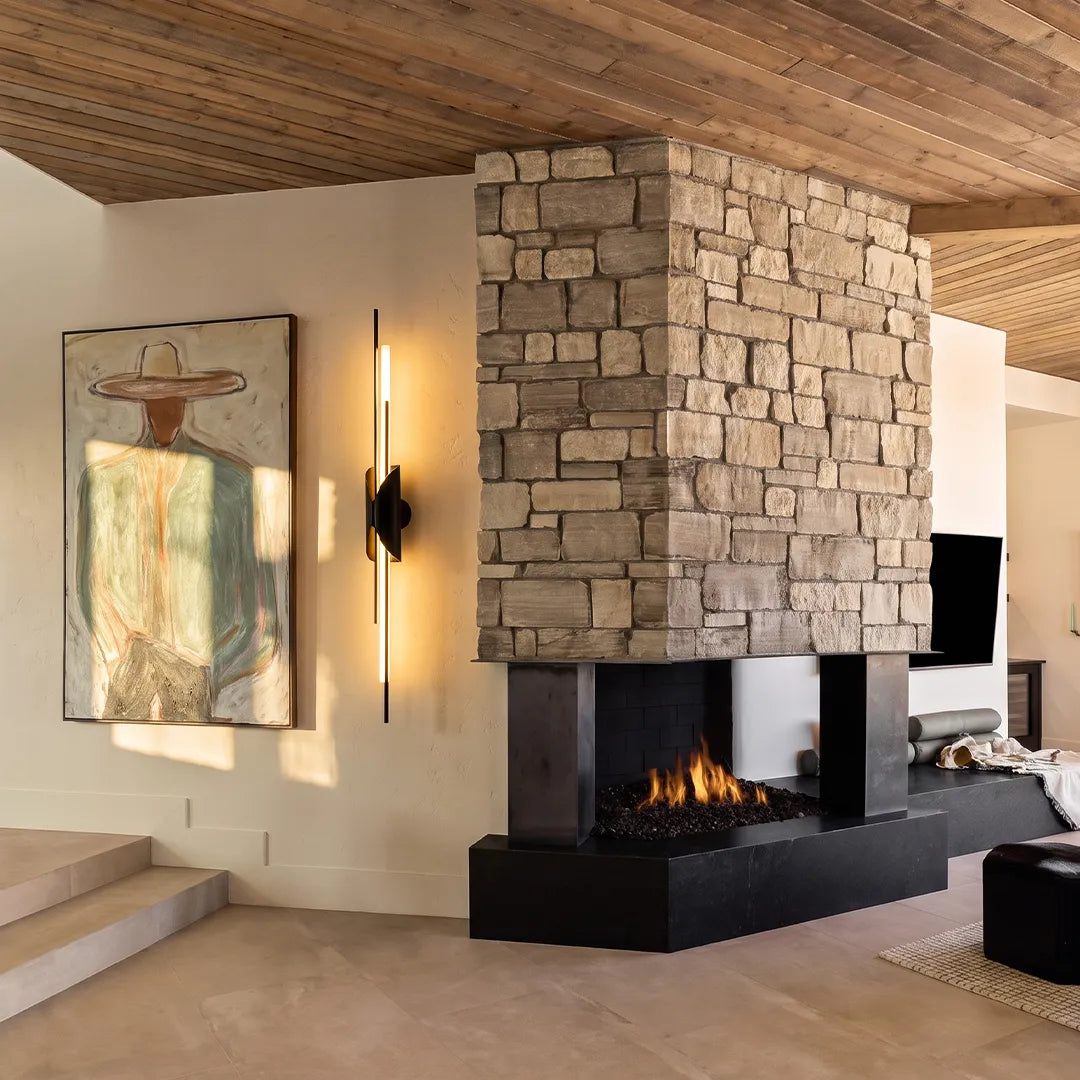 Brass wall sconce light beside a stone fireplace in a contemporary interior.