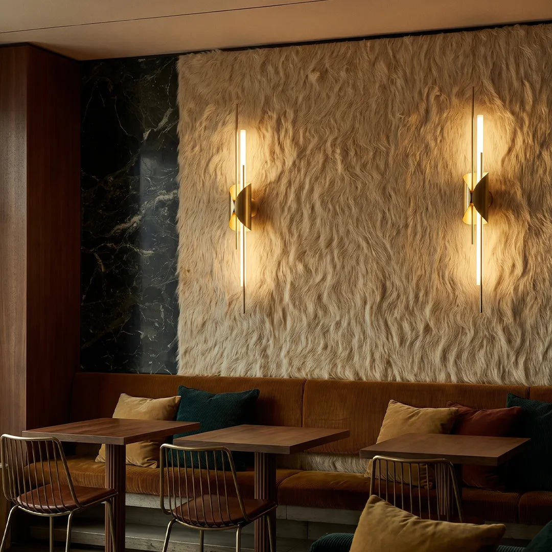Brass wall sconce light illuminating a textured feature wall in a cozy lounge area.