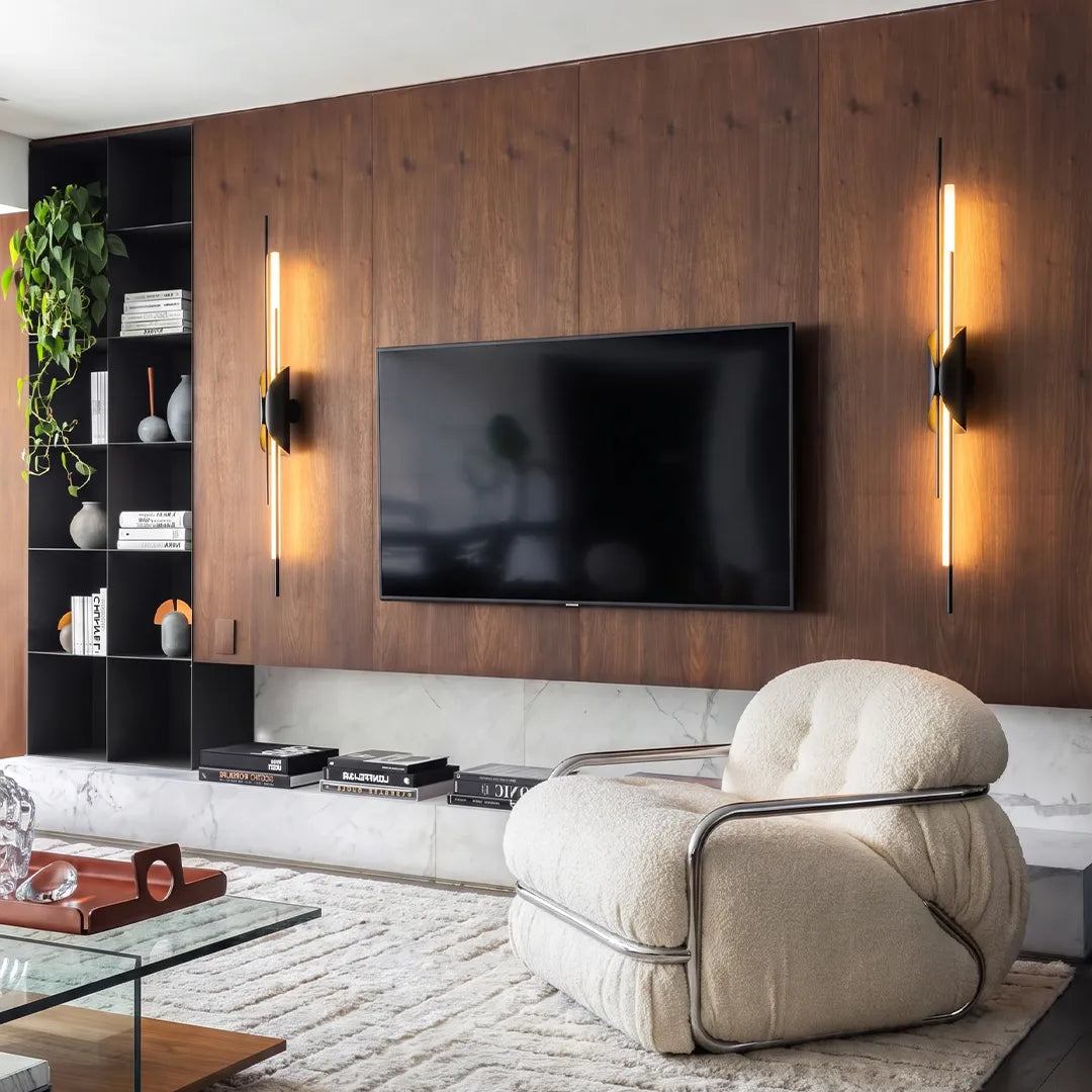 Brass wall sconce light flanking a TV in a modern living room with wood paneling.