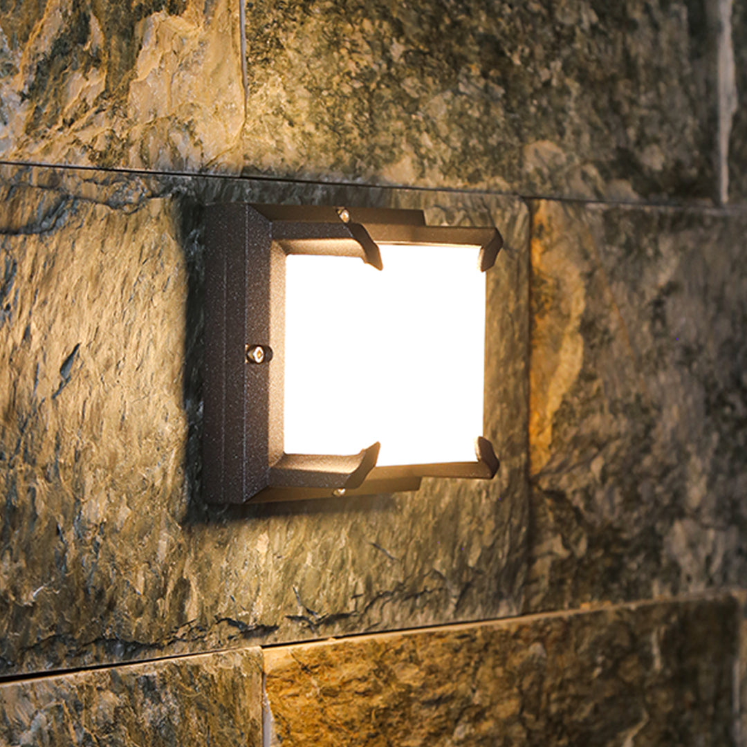 Close-up on the bright illumination from a decorative Black Outdoor Wall Light fixture mounted on a textured tan stone wall.