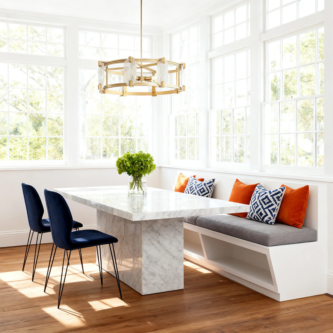 Round glass chandelier illuminating a bright sunroom with large windows and a white marble built-in bench seating area.