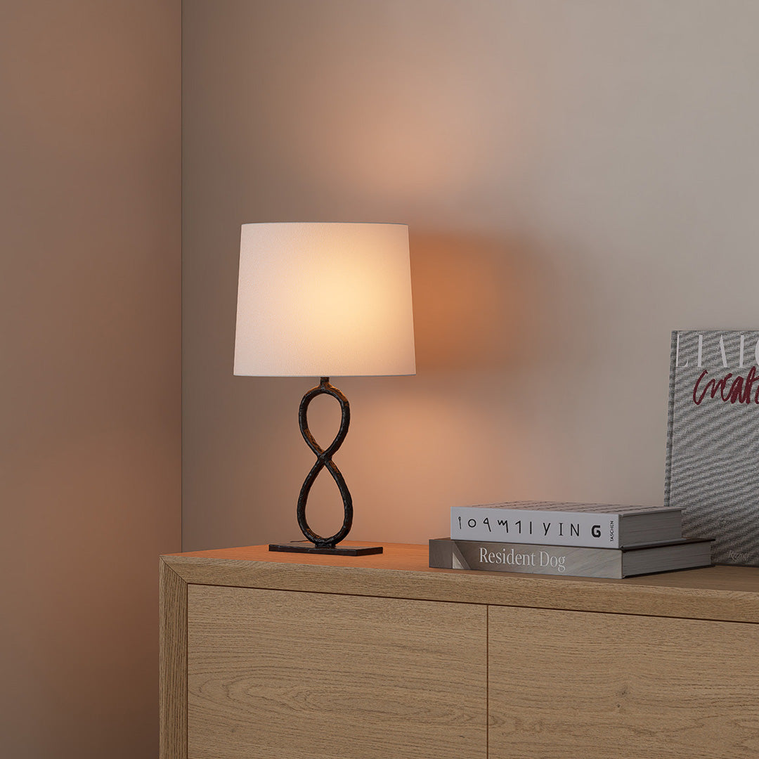 Bronze decorative table lamp with round fabric shade on modern cabinet in warm-toned room.