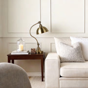 Bronze desk lamp placed beside a sofa in a bright living room.