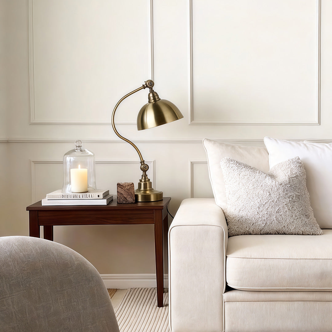 Bronze desk lamp placed beside a sofa in a bright living room.
