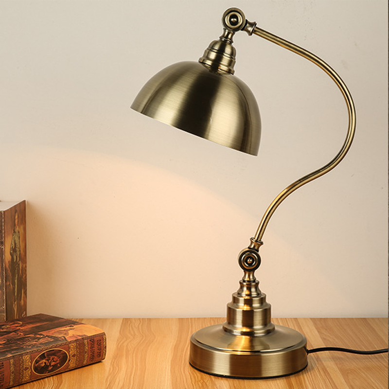 Bronze desk lamp turned on showing warm light on a tabletop.