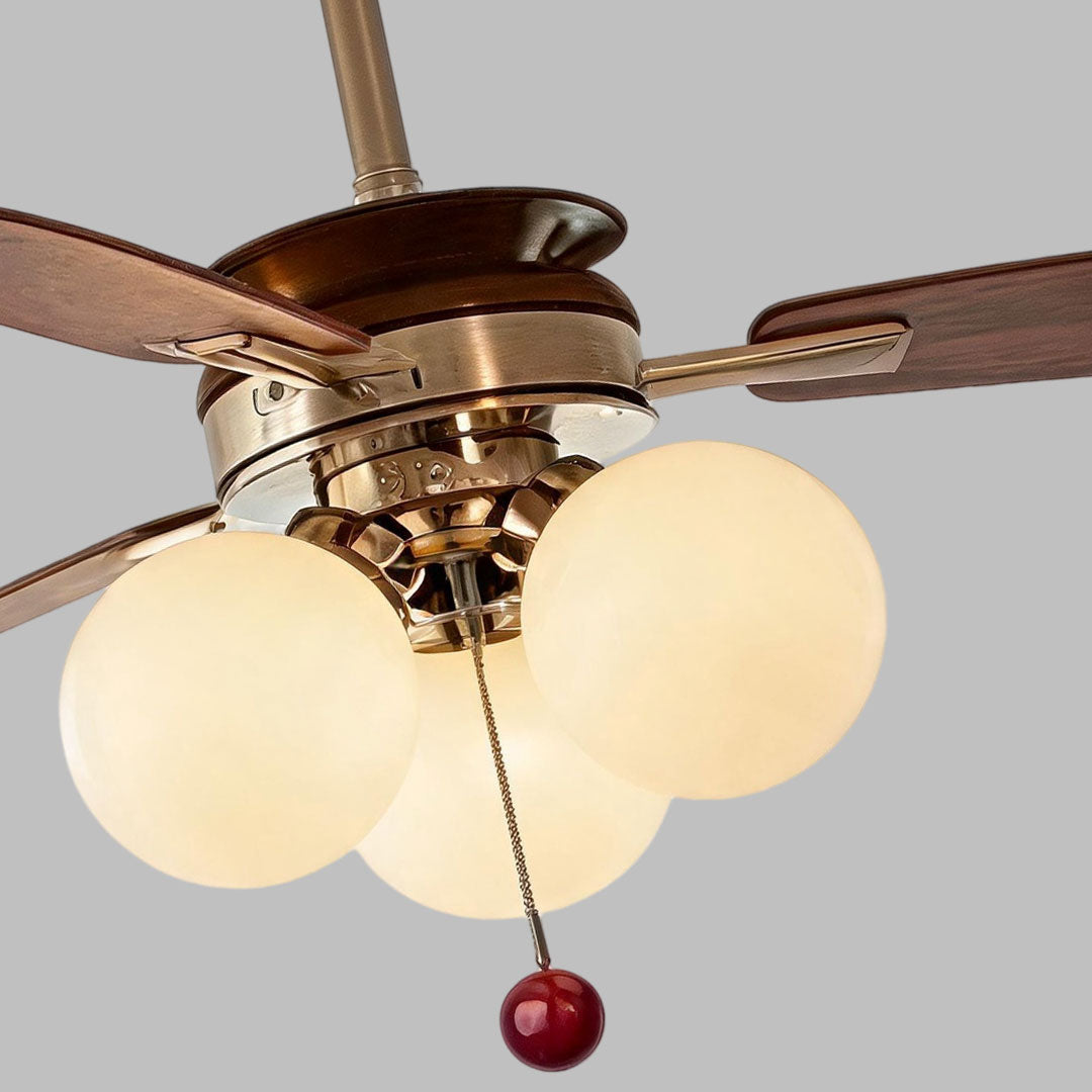 Close-up of indoor ceiling fan with light showing bronze hardware, walnut blades, and globe shades.