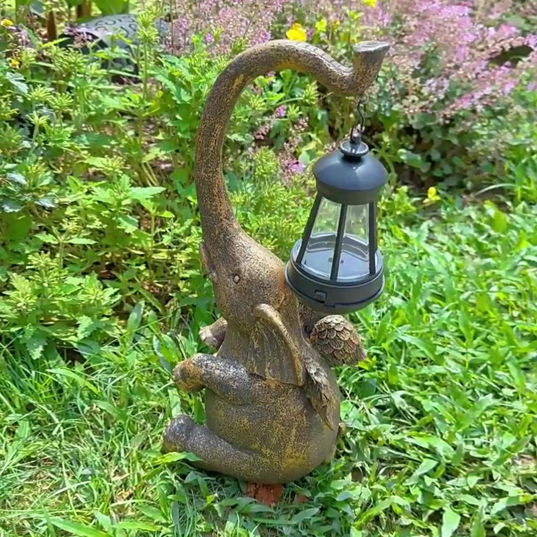 Bronze elephant garden sculpture with curved trunk holding lantern surrounded by flowering plants