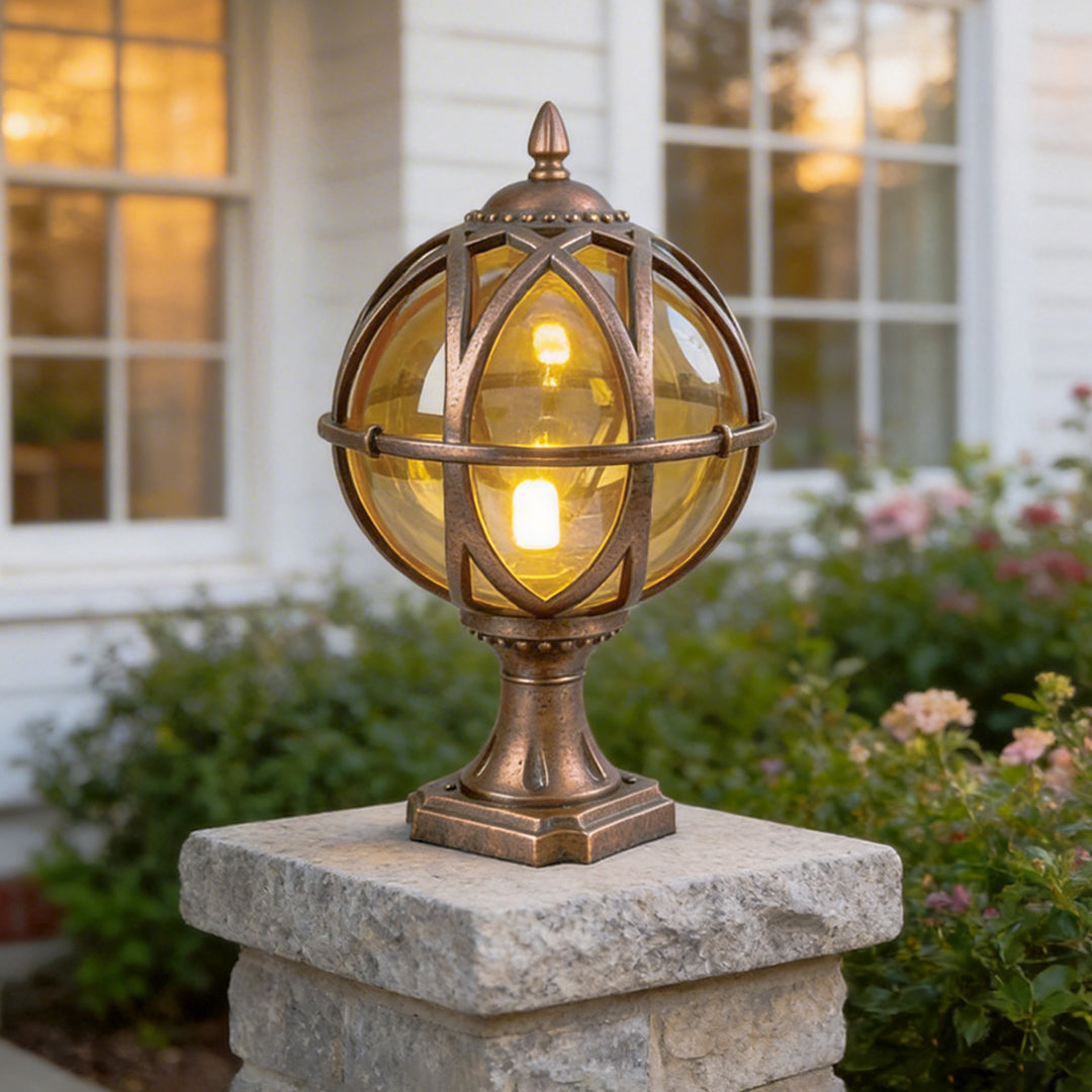 Bronze globe pillar light glowing on a stone post with a white traditional house background now.