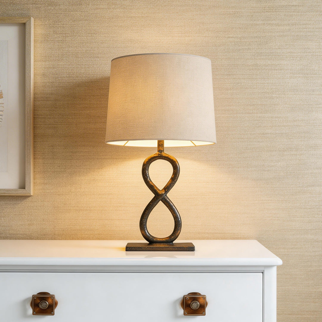 Elegant bronze metal table lamps with an infinity loop base and linen drum shade on a dresser.